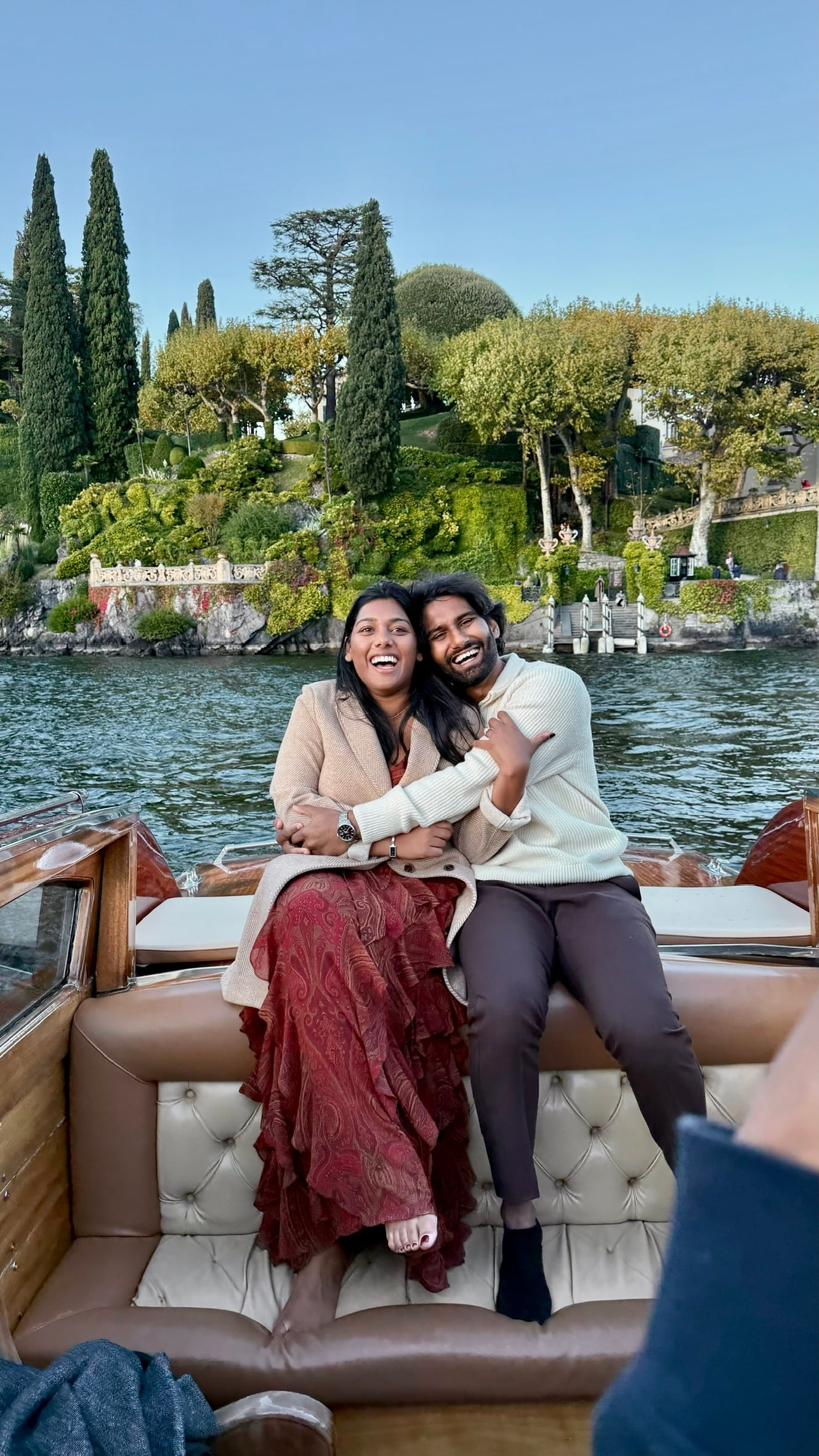 Esha & Anish laughing together on a wooden boat on Lake Como